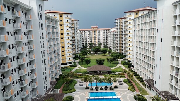 A high-rise residential building with multiple balconies, a central swimming pool, and surrounding greenery.