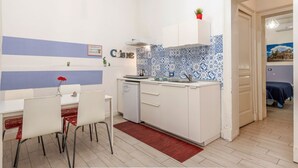 A compact kitchen with a dining area, white cabinets, a small refrigerator, and a tiled backsplash. - GuestHost - Central apartment Caronda street (Catania)
