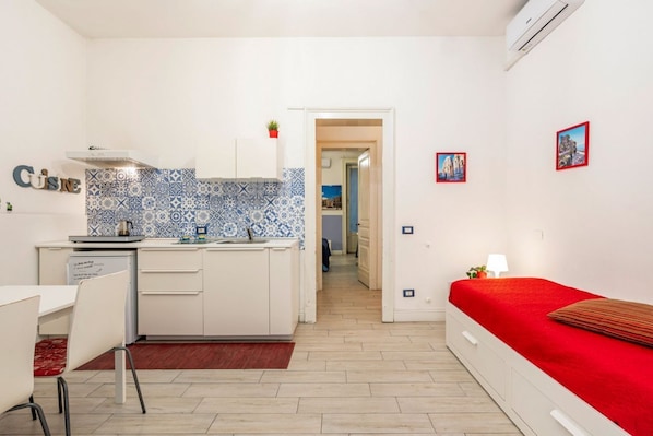 A compact room with a kitchenette, a dining area, and a bed.