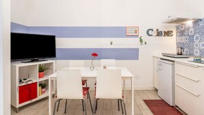 A compact kitchen with a dining area, a flat-screen TV, and a small refrigerator. - GuestHost - Central apartment Caronda street (Catania)
