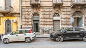 Two parked cars on a street with a building featuring arched windows and a balcony. - GuestHost - Central apartment Caronda street (Catania)