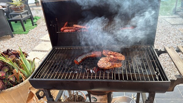 A barbecue grill with sausages and a steak being cooked.
