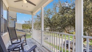 A covered porch with two rocking chairs, a ceiling fan, and a view of a residential street and trees. - Coastal Quarters in Bluffton - Dog Friendly! Bluffton Park Lowcountry Charmer (Bluffton)