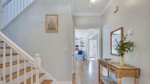 A hallway with a wooden staircase, a console table with a vase, and a framed picture on the wall. - Coastal Quarters in Bluffton - Dog Friendly! Bluffton Park Lowcountry Charmer (Bluffton)