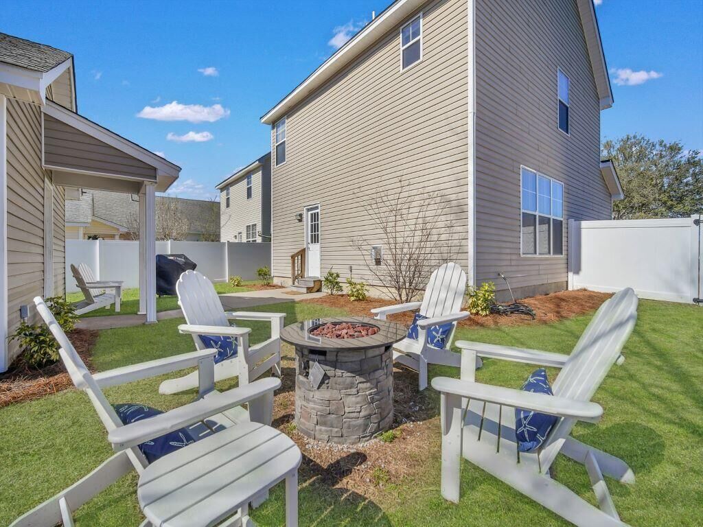 Een achtertuin met een vuurkorf, witte Adirondack-stoelen en een overdekt terras.