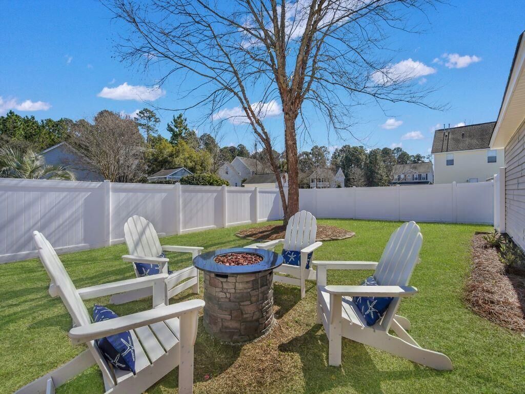 Un jardin avec un foyer en pierre, des fauteuils Adirondack blancs et un arbre.