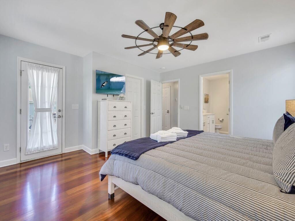 Ein Schlafzimmer mit Holzboden, einem Bett mit gestreifter Bettwäsche, einem Deckenventilator und einem Fernseher an der Wand.