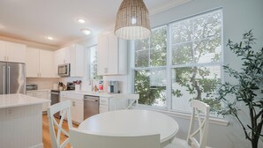 A modern kitchen with white cabinetry, a round dining table, and a hanging light fixture. - Coastal Quarters in Bluffton - Dog Friendly! Bluffton Park Lowcountry Charmer (Bluffton)
