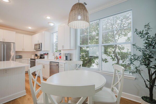 A modern kitchen with white cabinetry, a round dining table, and a hanging light fixture.