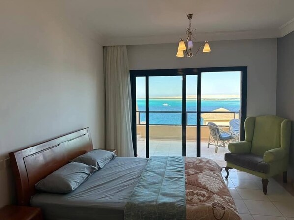 A hotel room with a bed, a chair, and a view of the sea through a sliding door.