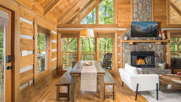 A log cabin interior with a stone fireplace, wooden dining table, and white sofa. - DreamForest 3BR, Firepit, Foosball, Banner Elk (Banner Elk)