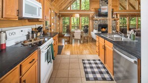 A spacious kitchen with wooden cabinets, a microwave, stove, and a stone fireplace. - DreamForest 3BR, Firepit, Foosball, Banner Elk (Banner Elk)