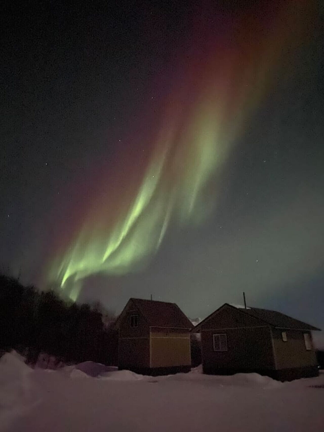 Uma casa com garagem em uma paisagem nevada sob um céu noturno com a Aurora Boreal.