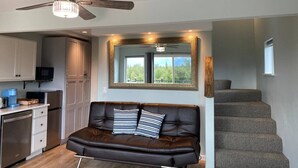 Un espace de vie moderne comprenant un canapé en cuir foncé, un ventilateur de plafond, un coin cuisine et un escalier.
