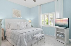 A bedroom with a bed, a TV, a window with curtains, and a bedside table. - Tivoli by the Sea 5286 (Miramar Beach)