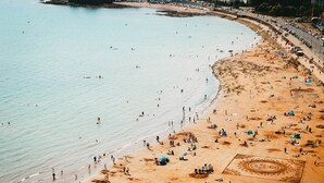 An aerial view of a beach with people, tents, and a sandy area with a circular pattern.