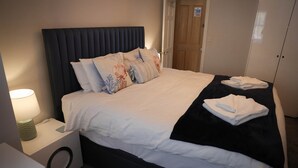 A neatly made bed with white linens and decorative pillows, a bedside table with a lamp, and a black throw blanket on the bed.