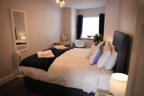 Un lit bien fait, avec une literie blanche et foncée, une table de chevet avec une lampe, une chaise et une fenêtre avec des rideaux.