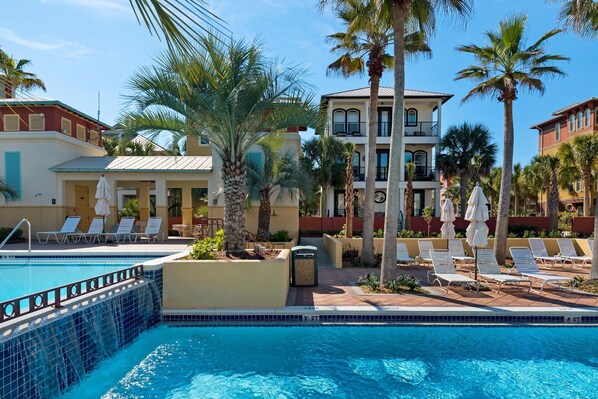 A pool area with lounge chairs and palm trees, surrounded by buildings with balconies.