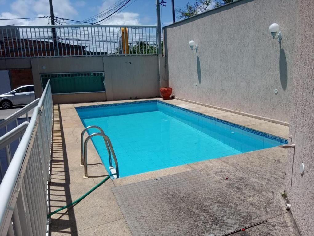 Une piscine rectangulaire à l’eau d’un bleu limpide, entourée d’une terrasse en béton et d’une rambarde en métal blanc.