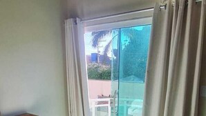 A hotel room with a bed, a wooden bench, a glass door leading to a balcony, and a view of the outdoors.