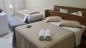 A hotel room with a large bed, a bedside table, a chair, a desk, a ceiling fan, and an air conditioning unit.