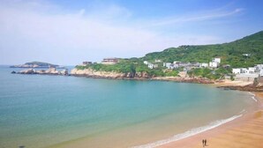 A coastal view with a sandy beach, calm sea, and a hillside with buildings. - Wudaoqing Guesthouse (Shengsi)