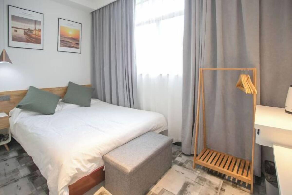 A hotel room with a bed, a bench, a wooden rack, a nightstand, and a wall with two framed pictures.