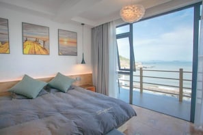 Et soveværelse med en stor seng, et natbord, en lampe og havudsigt fra en balkon.
