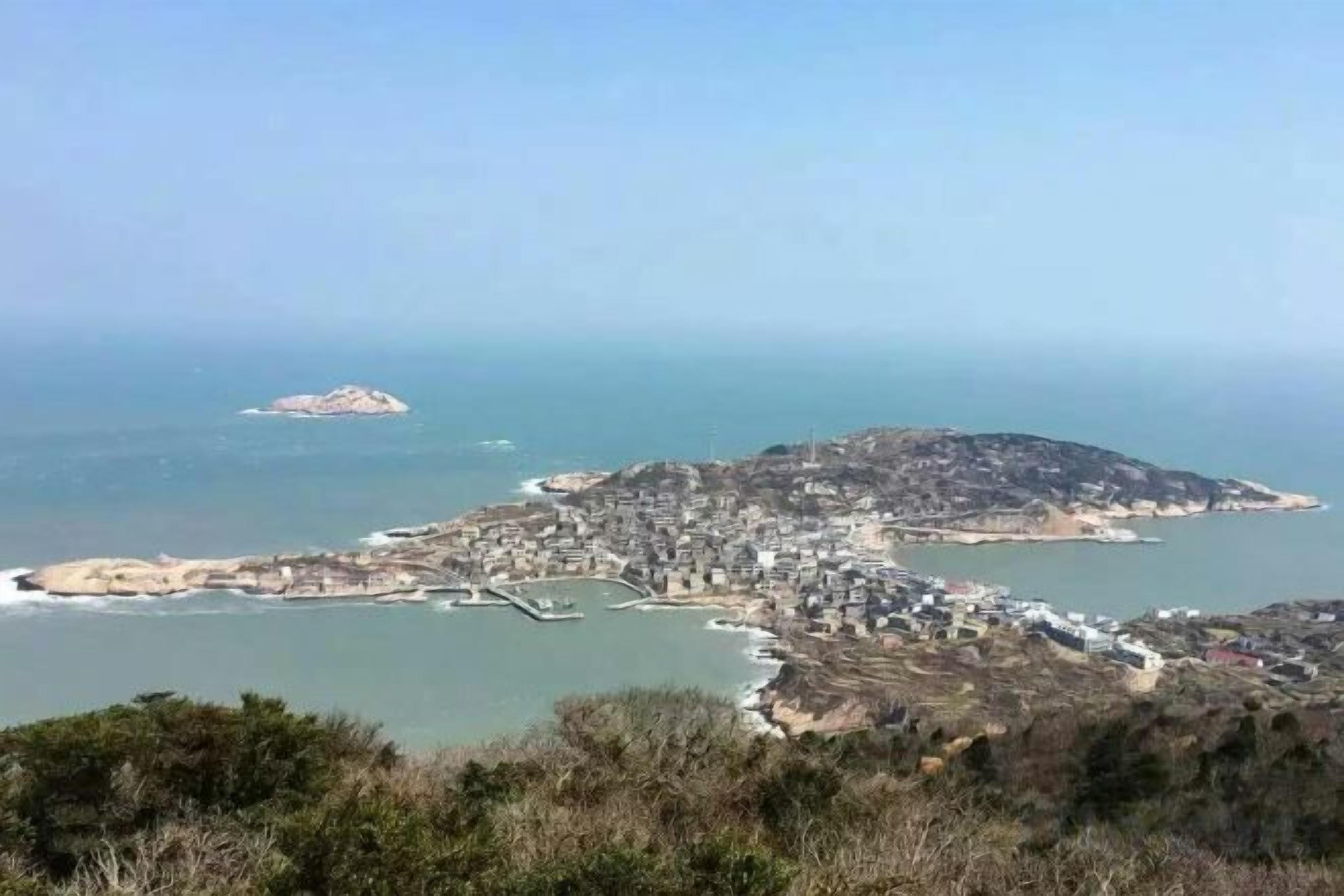 A coastal town with a marina, buildings, and a hilly landscape.