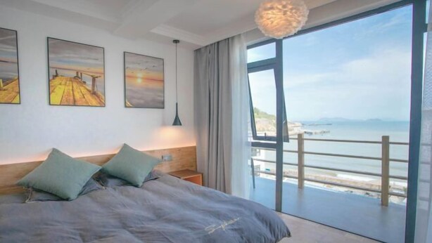 A bedroom with a large bed, a view of the sea through a balcony, and artwork on the wall. - Wudaoqing Guesthouse (Shengsi)