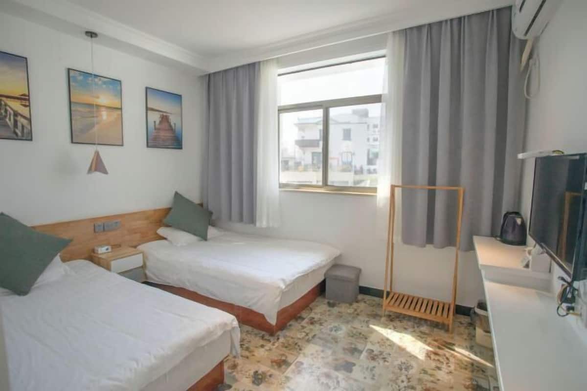 A hotel room with two beds, a TV, a desk, and a window with curtains.