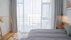 A bedroom with a bed, a wooden headboard, a hanging light fixture, a wooden bench, and a view through a window with curtains. - Wudaoqing Guesthouse (Shengsi)