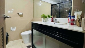 A modern bathroom with a glass shower enclosure, a white toilet, and a black vanity with a mirror. - OYO 1171 Raja Alea Residences (Bacoor City)