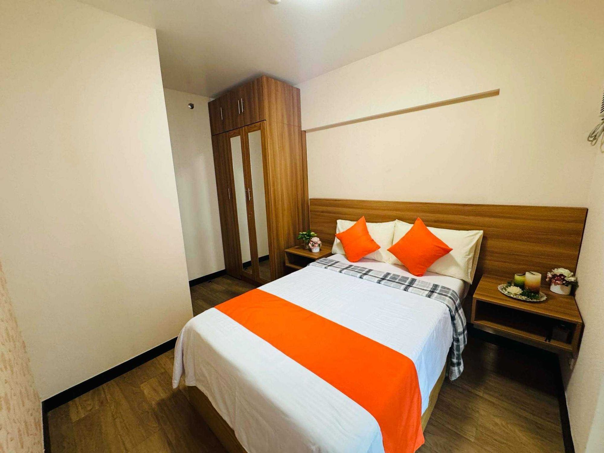 A hotel room with a bed, wooden wardrobe, bedside table, and a nightstand with a small plant.