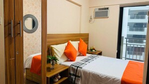 A hotel room with a wooden bed, a nightstand with a plant, a mirror, and a window with a view of a building. - OYO 1171 Raja Alea Residences (Bacoor City)