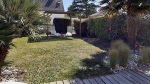 Ein Garten mit einer Holzterrasse, einer Pergola und einem Rasen.
