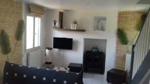 Ein Wohnzimmer mit einer Couch, einem flachbildfernseher an der Wand, einem Kamin und einer Treppe.
