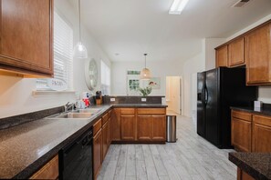 Eine moderne Küche mit Holzschränken, einem schwarzen Kühlschrank und einer Arbeitsplatte aus Granit.
