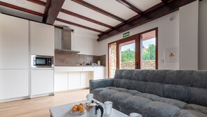 A modern kitchen with a built-in microwave, a stone wall, and a gray sofa in the living area. - Infinity Coast I by Fidalsa (Miengo)