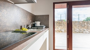 A modern kitchen with a stone wall backsplash, a sink with a faucet, a coffee maker, and a plate of grapes. There is a sign above the door reading "SALIDA". - Infinity Coast I by Fidalsa (Miengo)