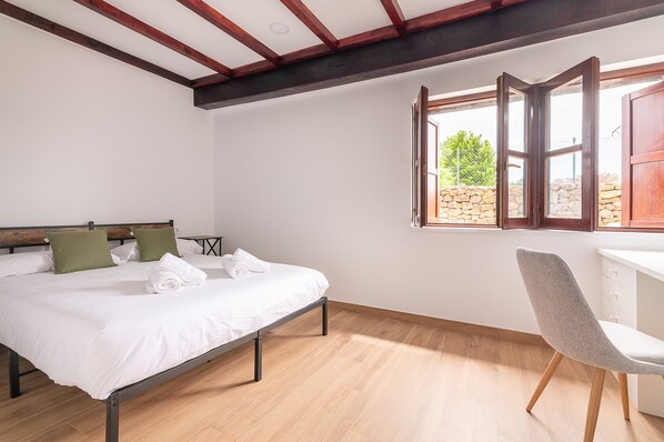 Une chambre à coucher avec un lit, un bureau et une chaise. Il y a une fenêtre avec une porte ouverte.