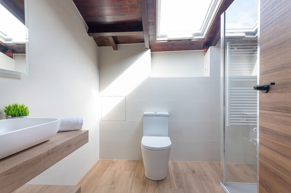 Une salle de bain moderne avec un puits de lumière, des toilettes blanches, un meuble-lavabo en bois et une cabine de douche en verre.