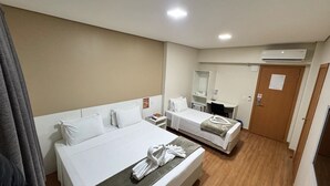A hotel room with two beds, a desk, a chair, a mirror, and an air conditioning unit. - Hotel Zandona (Blumenau)