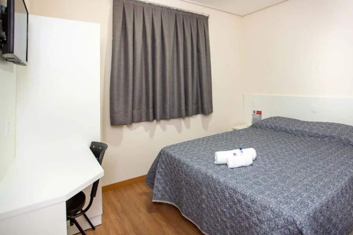 Une chambre d’hôtel avec un lit, un bureau, une chaise et une fenêtre avec des rideaux.