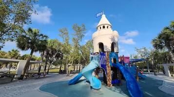 A playground with a slide and a play structure, surrounded by trees and a clear sky.