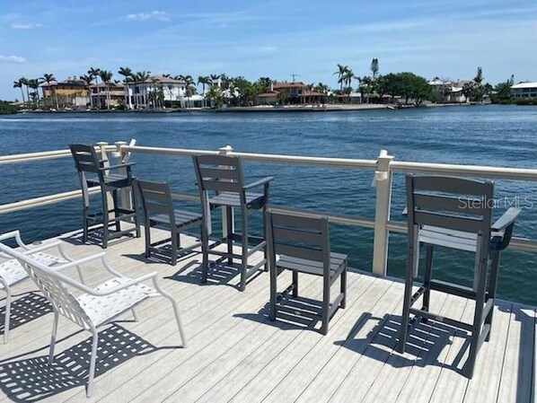 A deck with metal chairs and a table, overlooking a body of water with buildings in the background.