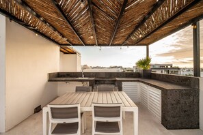 Een buitenkeuken met een tafel, stoelen, een barbecue en uitzicht op de stad.
