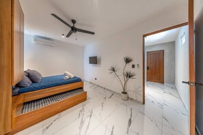 A modern bedroom with a bed, a ceiling fan, a TV, and a potted plant.