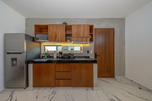 A compact kitchen with a built-in refrigerator, wooden cabinets, a microwave, and a sink.